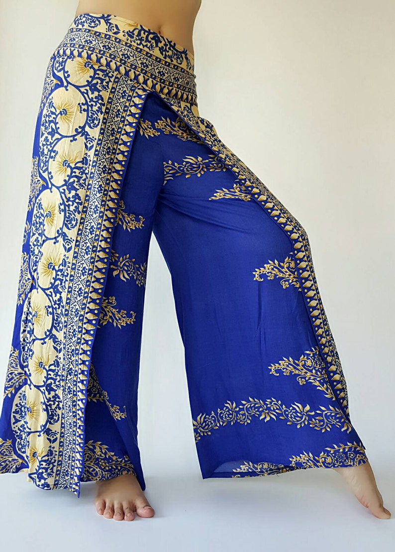 May include: Wide-leg trousers in blue with a gold and white floral print. The trousers have a wrap-around style and a high waist.