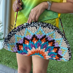 May include: A colorful, half-circle shaped handbag made of fabric with a unique, quilted design. The bag has a black and white trim and a long strap.