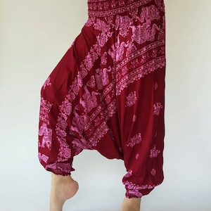 May include: Burgundy harem trousers with a pink elephant print. The trousers feature a wide, elasticated waistband and gathered ankles. The fabric drapes loosely, creating a comfortable silhouette. The elephant pattern is repeated throughout the design.