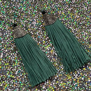 May include: A pair of green tassel earrings with silver metal accents. The earrings have a decorative design on the metal accents.