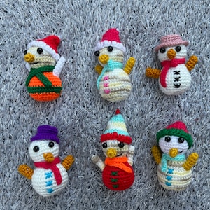 Puede incluir: Seis adornos de muñeco de nieve de crochet con sombreros y bufandas de diferentes colores. Los muñecos de nieve son todos blancos con ojos negros y botones.