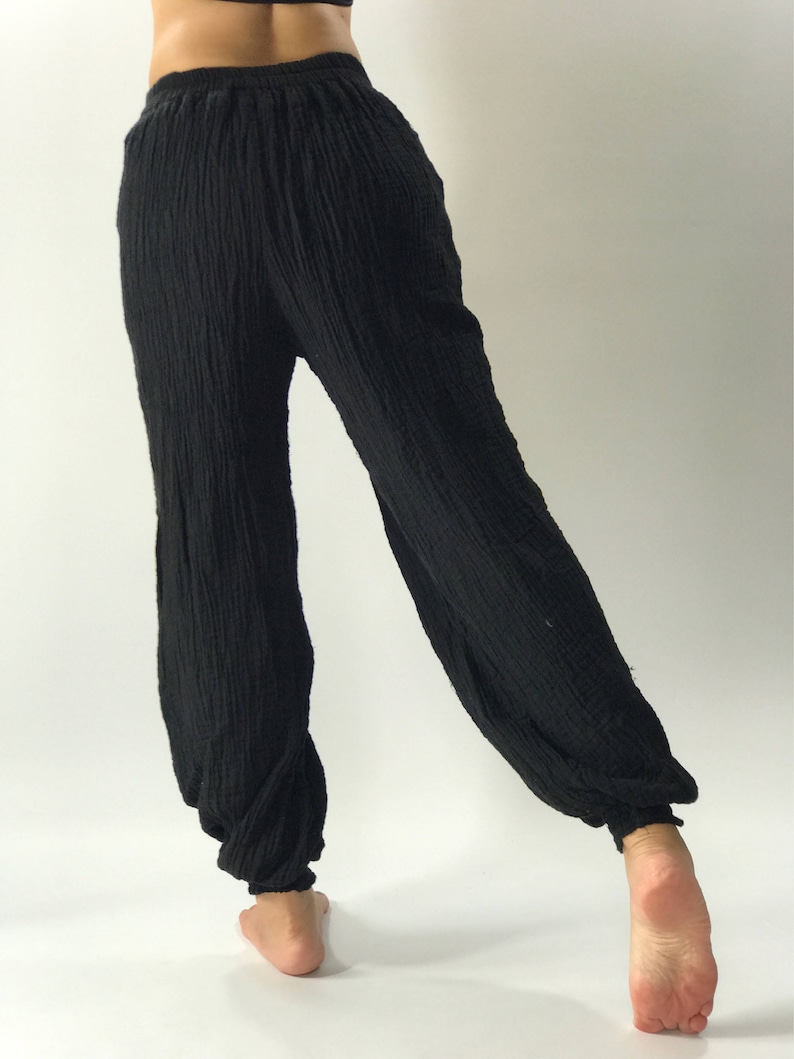 May include: Black, loose-fitting pants with a gathered elastic waistband. The pants are made of a soft, textured fabric.
