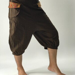 May include: Brown cotton pants with a unique design featuring a gathered hem and embroidered details on the pockets.