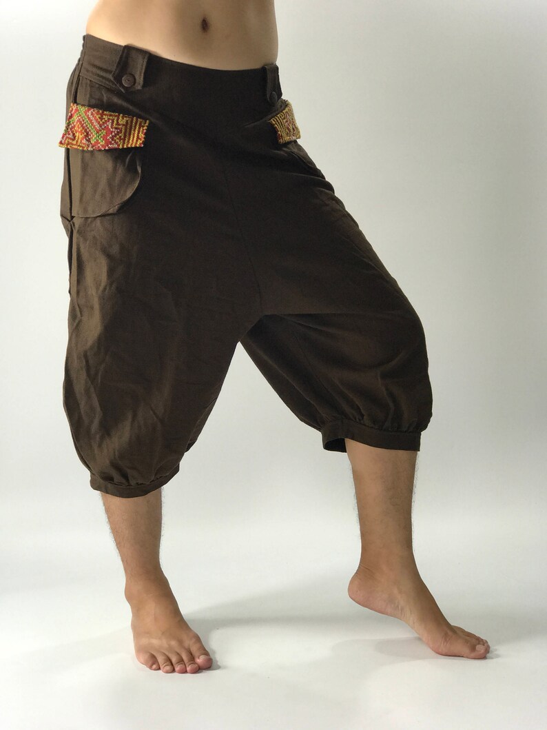 May include: Brown cotton pants with a unique design featuring a gathered hem and embroidered details on the pockets.