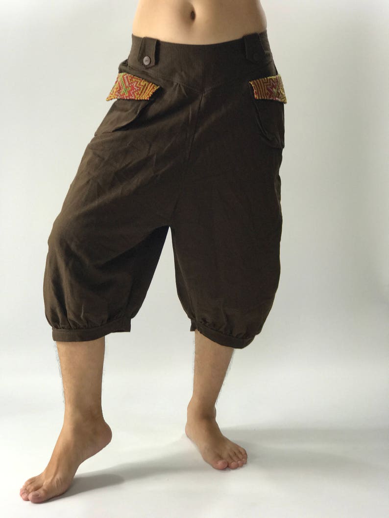 May include: Brown linen pants with a loose, wide leg and a gathered cuff at the bottom. The pants have two pockets with colorful embroidered trim.