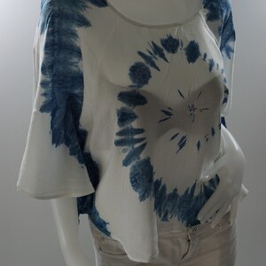 May include: A white and blue tie-dye top with a round pattern. The top has a scoop neck and short sleeves. The model is wearing the top with beige shorts.
