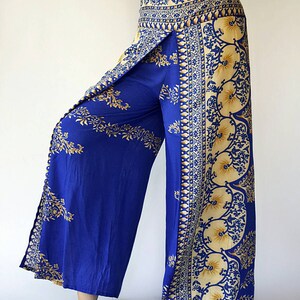 May include: Wide-leg trousers in blue with a gold and white floral print. The trousers have a wrap-around style and a high waist.