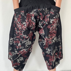 May include: Black pants with a red and white floral print. The pants have a wide leg and a drawstring waist.