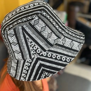 Puede incluir: Sombrero de cubo negro y blanco con un patrón geométrico. El sombrero está hecho de tejido tejido.
