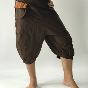 May include: Brown cotton pants with a unique design. The pants have a wide leg and a gathered cuff at the bottom. The pockets have a colorful embroidered trim.