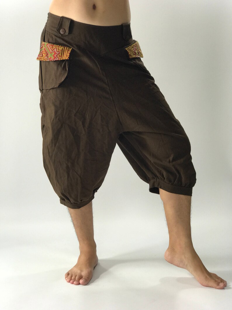 May include: Brown cotton pants with a unique design. The pants have a wide leg and a gathered cuff at the bottom. The pockets have a colorful embroidered trim.