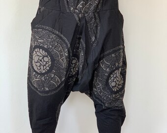 May include: Black harem trousers featuring a grey mandala design. These cropped trousers have a drawstring waist and pockets. The fabric looks lightweight, suitable for warmer weather. The length is to the calf.