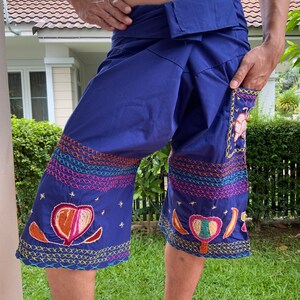 May include: Blue cotton trousers with colourful embroidery. The trousers have a wide waistband and a loose fit. The embroidery features flowers, stars, and other designs.