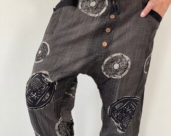May include: Black and beige patterned trousers with a drawstring waist and button fastening. The trousers feature a unique design with circular patterns and a textured fabric.