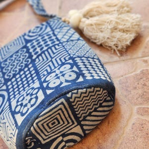 Peut inclure: Un sac à main à motifs bleus et blancs avec une sangle assortie et un pompon crème. Le sac présente des motifs géométriques et une forme arrondie, parfait pour transporter l'essentiel.