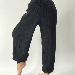 May include: Black, loose-fitting pants with a gathered elastic waistband. The pants are made of a soft, crinkled fabric.