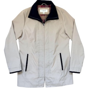 May include: A beige jacket with a black collar and a plaid lining. The jacket has a zip fastening and two pockets with black trim.