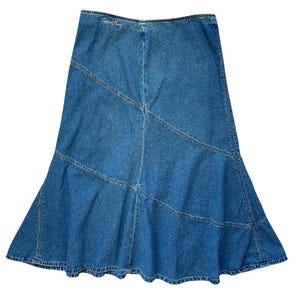 Peut inclure: Jupe en jean bleu avec un ourlet évasé. La jupe présente un design patchwork avec des coutures diagonales et des coutures visibles. Le texte "Sweet Child" est brodé sur la ceinture. La jupe est en jean délavé moyen.