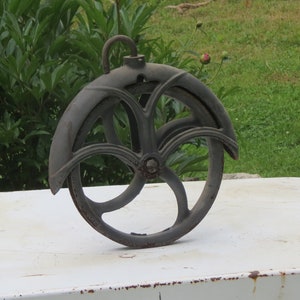 May include: A black cast iron pulley with a three-spoke wheel and a hook at the top.