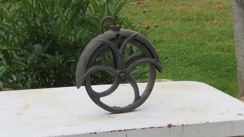 May include: A black cast iron pulley with a three-spoke wheel and a hook at the top.