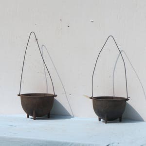 May include: Two small black cast iron pots with wire handles. The pots are sitting on a light blue surface.
