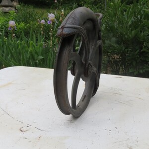 May include: A rusty metal wheel with a decorative design. The wheel is made of cast iron and has a dark brown color.