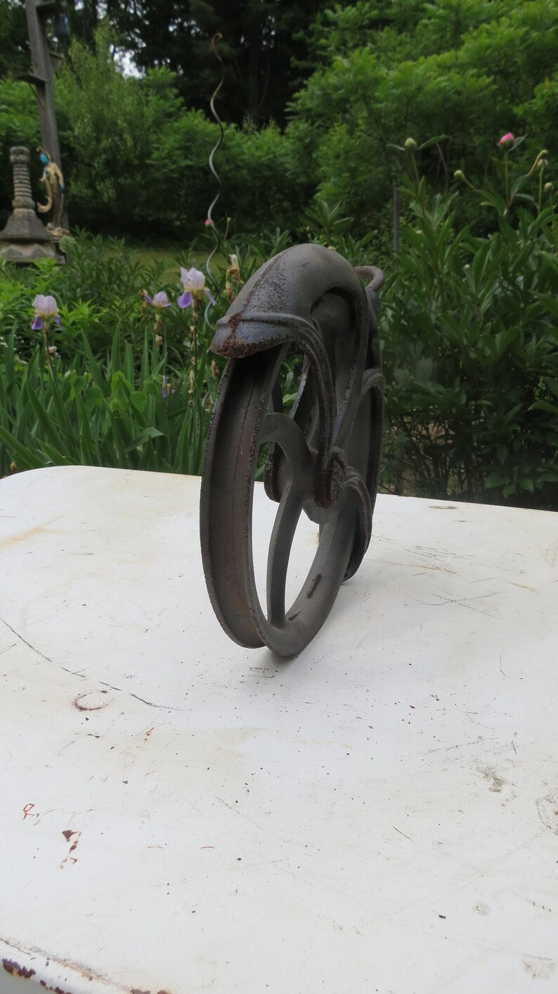 May include: A rusty metal wheel with a decorative design. The wheel is made of cast iron and has a dark brown color.