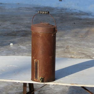 May include: A rusty metal container with a wooden handle and a spout. The container is sitting on a white table.