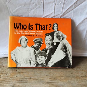 May include: An orange book titled "Who Is That?" The Late Late Viewer's Guide to the Old Old Movie Players by Warren B. Meyers. The cover features black and white photos of actors.