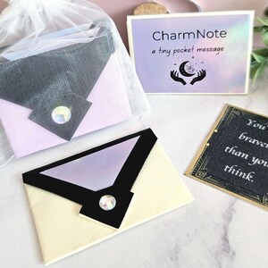 May include: An assortment of small, decorative envelopes in various colors, including cream, lavender, and gray, with a sparkling gem accent. One envelope is in a sheer bag. A card reads "CharmNote a tiny pocket message". Another card says "You're braver than you think."