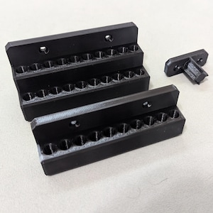 May include: Black 3D-printed tool organizers. The image shows three stacked organizers with multiple small holes, and a separate connector piece. The organizers are designed to hold small tools or parts, and are made of a matte black material.