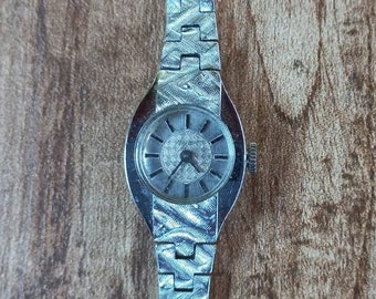 May include: A silver wristwatch with a round face and a silver metal band. The watch has a white face with black hour and minute hands and black markings.