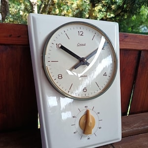 May include: A vintage white kitchen timer with a clock face and a timer dial. The clock face has black hands and the word "Exact". The timer dial is tan and has numbers from 0 to 60.