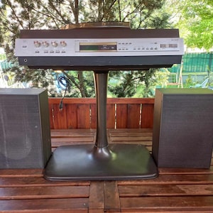 May include: A black stereo system with two speakers and a turntable on a black stand. The stereo system is on a wooden table.