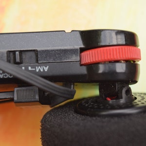 Pode incluir: Close-up de um r&aacute;dio preto com um bot&atilde;o vermelho e um cabo preto. O r&aacute;dio tem um r&oacute;tulo que diz "AM-T" e "LOCAL DX".