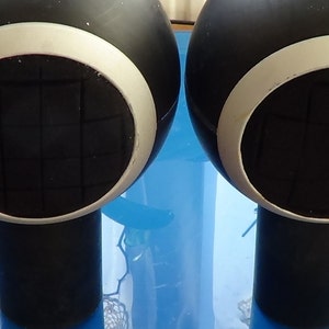 May include: Two black and white round objects with a white ring around the center. The center of each object has a black circle with a grid pattern.