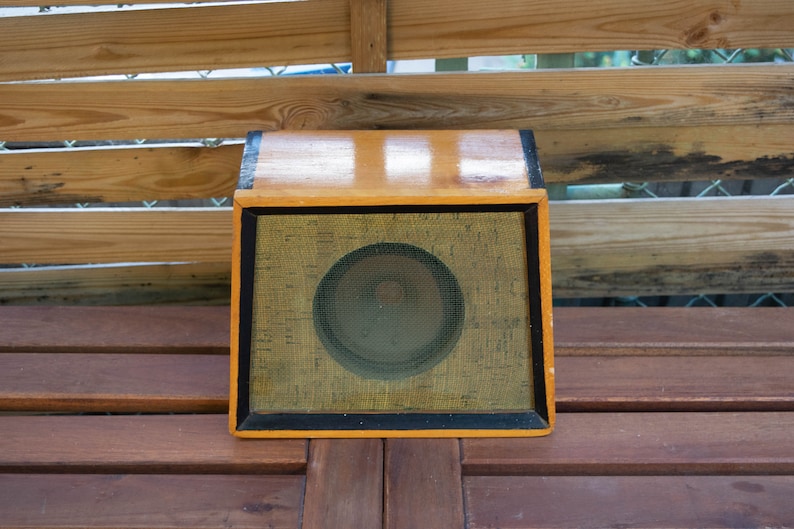 K&ouml;nnte beinhalten: Ein Vintage-Lautsprechergeh&auml;use aus Holz mit rechteckiger Form. Der Lautsprecher hat einen hellbraunen Holzrahmen mit einem schwarzen Rand um das Lautsprechergitter. Das Lautsprechergitter ist beige mit einem kreisf&ouml;rmigen Lautsprecher in der Mitte.