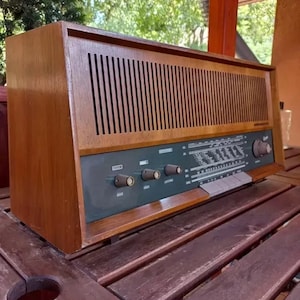 May include: A vintage wooden radio with a green front panel and a woodgrain finish. The radio has a dial with numbers and letters, and several knobs for adjusting the volume and other settings. The radio is sitting on a wooden table.