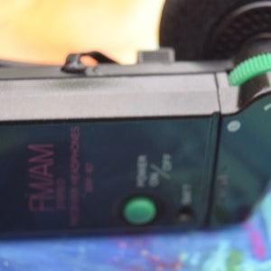 Pode incluir: Um fone de ouvido est&eacute;reo FM/AM Sony preto com um bot&atilde;o de volume verde e um bot&atilde;o de energia verde. Os fones de ouvido t&ecirc;m um r&oacute;tulo rosa e branco que diz "FM/AM Stereo Headphones".