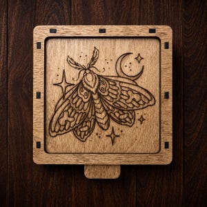May include: A square wooden box with a laser-engraved design on the lid. The artwork features a detailed moth centred between a crescent moon and several four-pointed stars. The wood has a natural light brown grain and dark joinery details.
