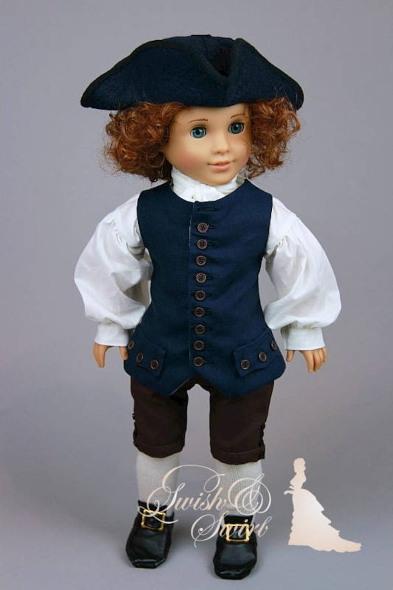 K&ouml;nnte beinhalten: Eine Puppe, die eine marineblaue Weste mit braunen Kn&ouml;pfen, ein wei&szlig;es Hemd, braune Shorts, wei&szlig;e Socken und schwarze Schuhe tr&auml;gt. Die Puppe tr&auml;gt einen schwarzen Hut und hat lockiges rotes Haar.