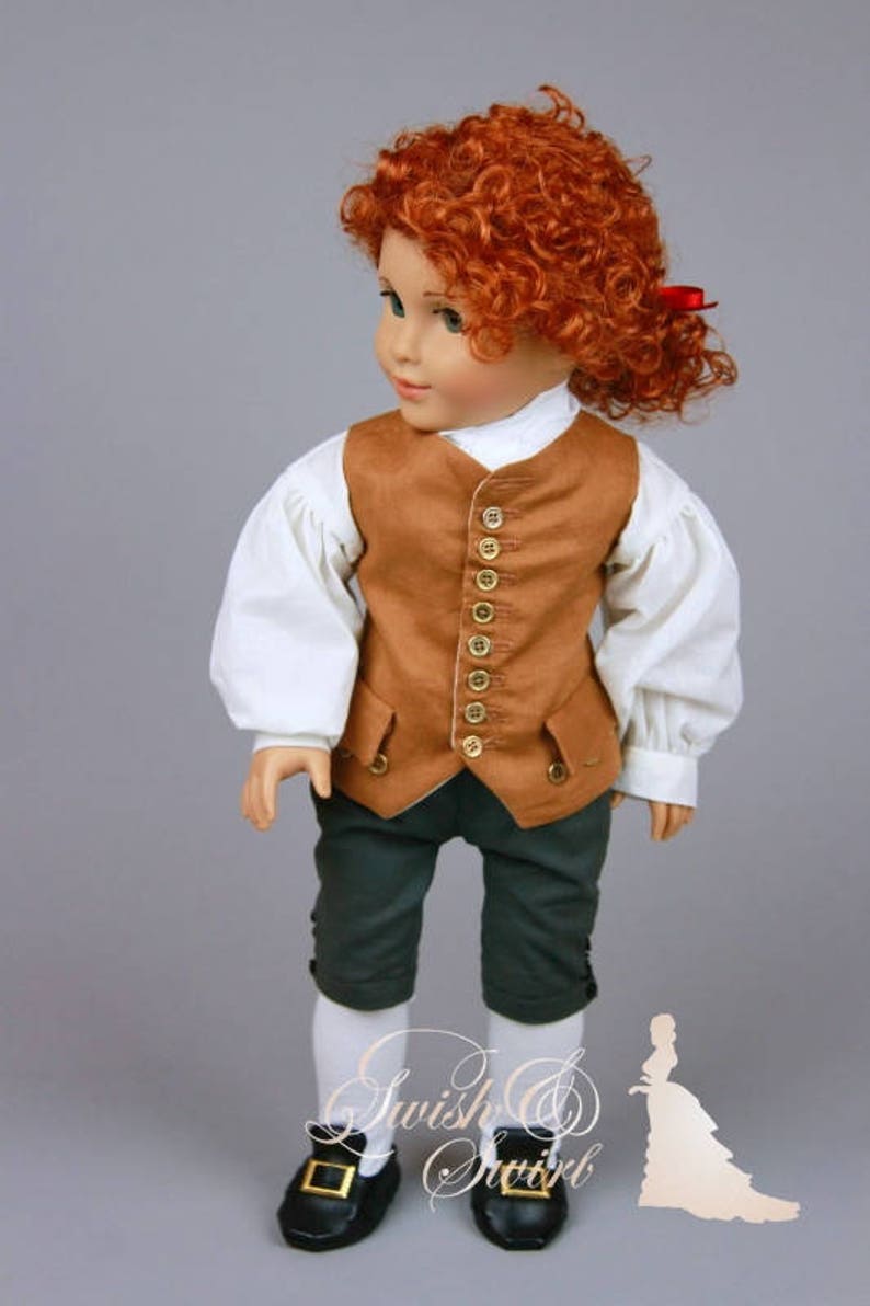 K&ouml;nnte beinhalten: Eine Puppe tr&auml;gt eine braune Weste mit goldenen Kn&ouml;pfen, ein wei&szlig;es Hemd mit Puff&auml;rmeln, eine gr&uuml;ne Hose und schwarze Schuhe. Die Puppe hat rote lockige Haare und tr&auml;gt ein rotes Band.