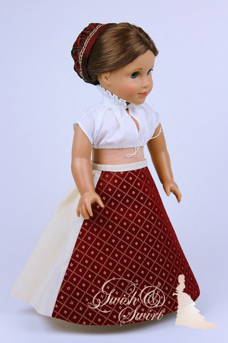 May include: A doll wearing a white crop top with a ruffled collar and a red patterned skirt. The skirt has a diamond pattern with gold accents. A matching red headband completes the outfit. The doll is a classic toy.
