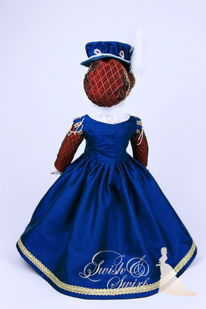 May include: A doll wearing a historical costume, featuring a royal blue dress with a full skirt and gold trim. The bodice has red and gold sleeves. A matching hat with a red net and blue trim is on the doll's head. A white feather is attached to the hat.