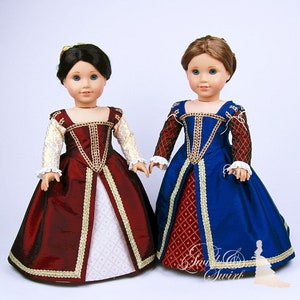 May include: Two dolls wearing Renaissance-style gowns. One doll is in a burgundy dress with gold trim and white sleeves. The other doll is in a blue dress with burgundy sleeves and gold trim. Both dresses have a square neckline and full skirt.