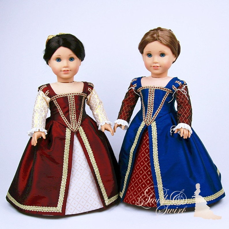May include: Two dolls wearing Renaissance-style gowns. One doll is in a burgundy dress with gold trim and white sleeves. The other doll is in a blue dress with burgundy sleeves and gold trim. Both dresses have a square neckline and full skirt.