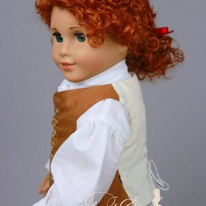 K&ouml;nnte beinhalten: Eine Puppe mit lockigem rotem Haar, die ein wei&szlig;es Hemd mit Puff&auml;rmeln und eine braune Weste mit goldenen Kn&ouml;pfen tr&auml;gt. Die Puppe tr&auml;gt eine gr&uuml;ne Hose und hat ein rotes Band im Haar.