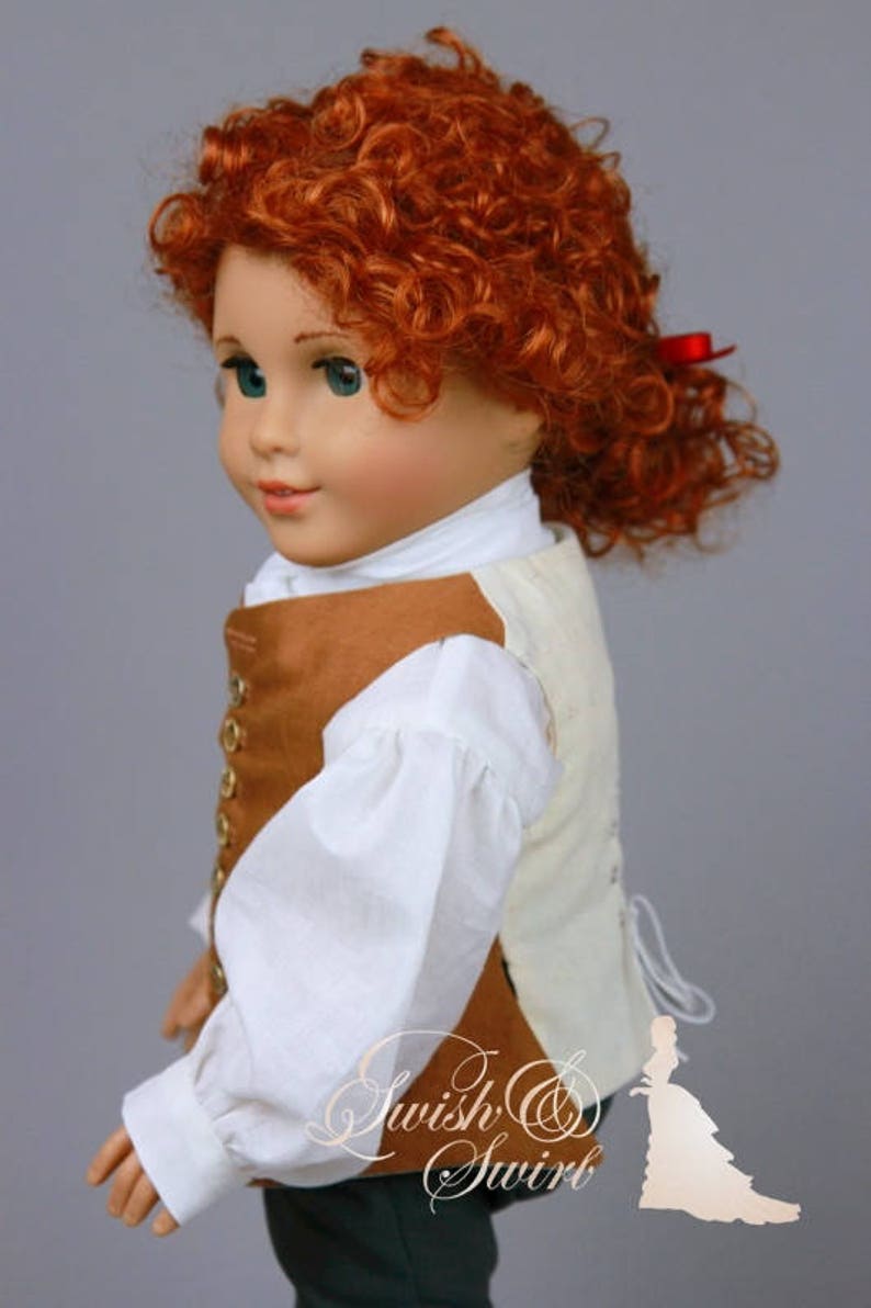 K&ouml;nnte beinhalten: Eine Puppe mit lockigem rotem Haar, die ein wei&szlig;es Hemd mit Puff&auml;rmeln und eine braune Weste mit goldenen Kn&ouml;pfen tr&auml;gt. Die Puppe tr&auml;gt eine gr&uuml;ne Hose und hat ein rotes Band im Haar.