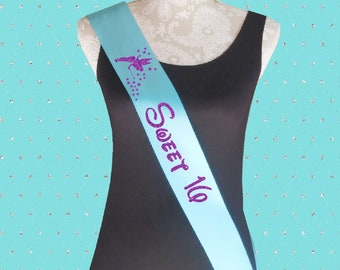 Könnte beinhalten: Ein hellblaues Satinband mit glitzerndem violettem Schriftzug "Sweet 16" und einem glitzerndem Tinkerbell-Design in Violett.