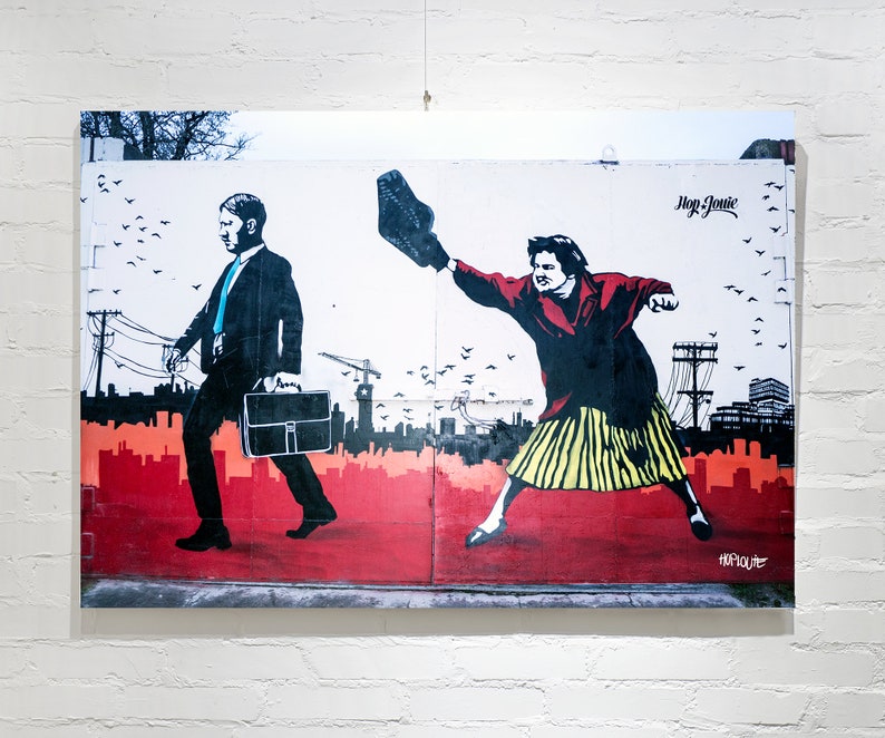 May include: A street art mural depicting two figures. A man in a suit walks to the right, carrying a briefcase. A woman in a red jacket and yellow skirt throws a shoe to the left. The mural is painted on a white wall with red, orange, and yellow accents. The text "Hop Louie" is visible in the upper right corner.